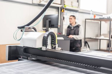 Matbaa işçisi teknisyeni büyük CNC bilgisayar sayısal kontrol baskı ve kesme makinesi üzerinde çalışıyor
