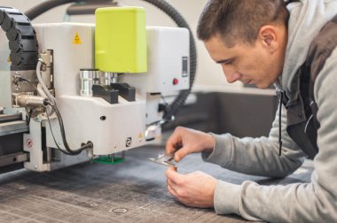 Elektrik mühendisi, büyük CNC bilgisayar sayısal kontrol yazdırma ve kesme makinesinde kafa kesen bir bıçağı tamir ediyor