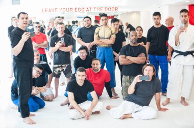 Dojo spor salonundaki çok ırklı spor öğrencilerinden oluşan büyük bir grup dövüş sanatları seminerinde cep telefonuyla video izleyip, dinliyor ve kaydediyor. Ön görünüm