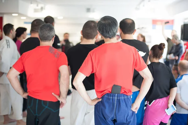 Large multiethnic international group of sport students in gym watches, listens and learns at a martial arts seminar. Back rear view