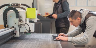 İki matbaa işçisi büyük CNC bilgisayar sayısal kontrol baskı ve kesme makinesi üzerinde çalışıyor