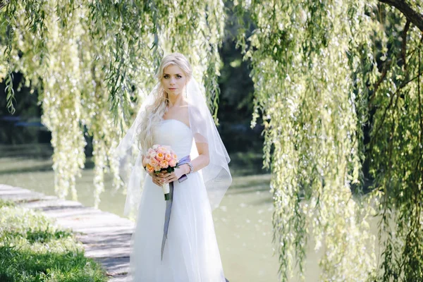 Elegante donna in abito da sposa e velo con un mazzo di rose su uno sfondo di salice — Foto Stock