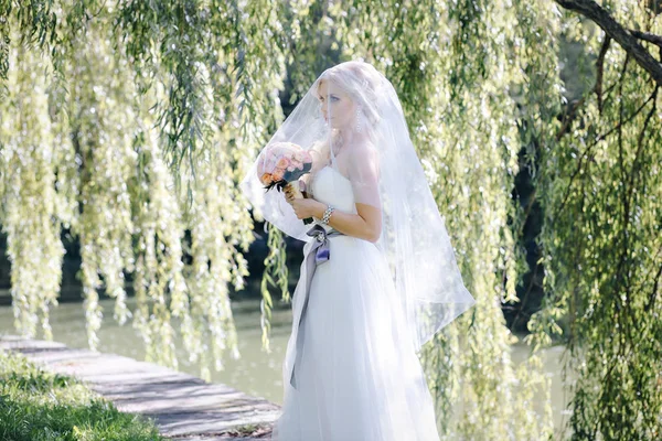 Elegante donna in abito da sposa e velo con un mazzo di rose su uno sfondo di salice — Foto Stock