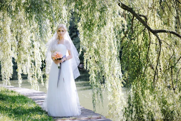 Elegante donna in abito da sposa e velo con un mazzo di rose su uno sfondo di salice — Foto Stock