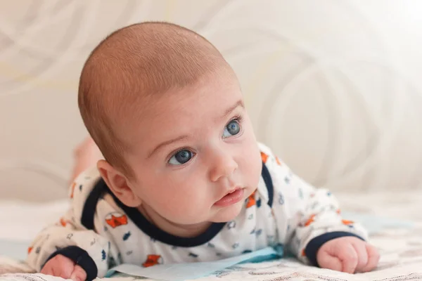 2 aylık büyük mavi gözlü ve uzun kirpikli sevimli erkek bebek portresi. Sevimli bebek karnının üstünde yatıyor ve şaşkınlıkla yüzünü çeviriyor. — Stok fotoğraf