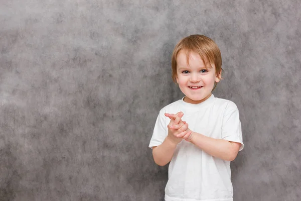 Мальчик со счастливой улыбкой на лице радостно хлопает в ладоши. Портрет на сером фоне. Летний стиль — стоковое фото