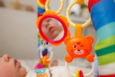 Bebek aynadaki yansımasını görüyor oyun minderinde.