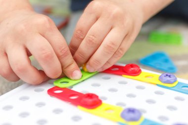 Mozaikte çocuk eli renkli vidayı sıkılaştırır. Çocuklarda el motorunun geliştirilmesi için aygıtlarla oynayan çocuk