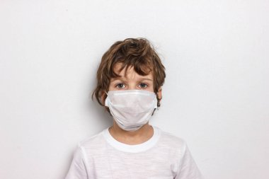 Beyaz arka planda beyaz maskeli tatlı kıvırcık çocuk. Coronavirus salgınıyla savaş. Aşı aranıyor.