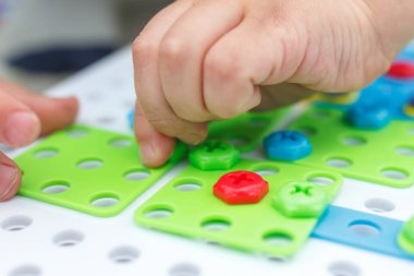 Mozaikte çocuk eli renkli vidayı sıkılaştırır. Çocuklarda el motorunun geliştirilmesi için aygıtlarla oynayan çocuk