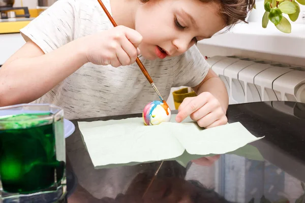 Мальчик окунул яйцо в стакан с краской. Мальчик рисует пасхальные яйца — стоковое фото