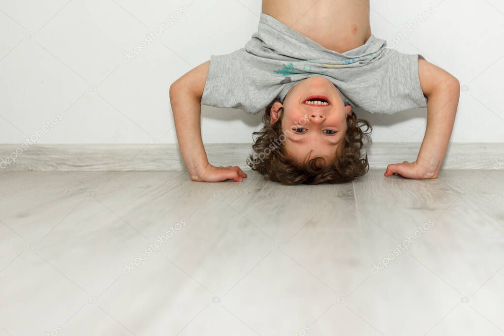 Little smiling cute child having fun standing by hands upside down head feeling positive emotion laughing funny baby child rejoicing on white wall background
