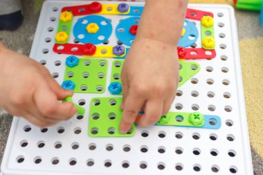 Mozaikte çocuk eli renkli vidayı sıkılaştırır. Çocuklarda el motorunun geliştirilmesi için aygıtlarla oynayan çocuk.