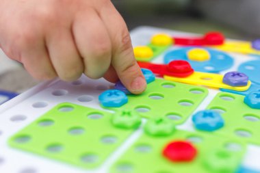 Mozaikte çocuk eli renkli vidayı sıkılaştırır. Çocuklarda el motorunun geliştirilmesi için aygıtlarla oynayan çocuk