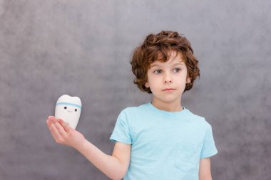 Şirin kıvırcık oğlan büyük diş tutuyor. Çocuk sağlığı ve ilaç kavramı