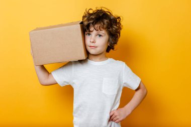 Kıvırcık Çocuk omzunda bir karton kutu tutuyor. Yemek teslimatı kavramı, online alışveriş.