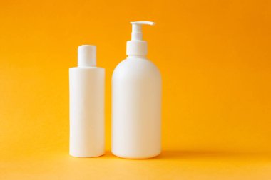 Kozmetik, nemlendirici, iki beyaz plastik şişe duş jeli ve sarı arka planda şampuan. Vücut ve saç bakım ürünleri seti.