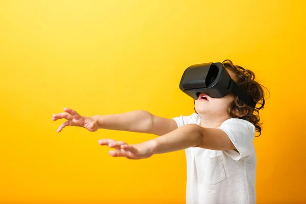 Close-up of little boy in virtual reality headset with arms extended forward. Boy wearing virtual reality glasses and white tshirt at yellow background