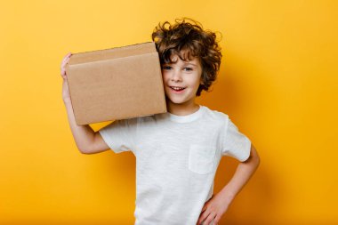 Kıvırcık Çocuk omzunda bir karton kutu tutuyor. Yemek teslimatı kavramı, online alışveriş.