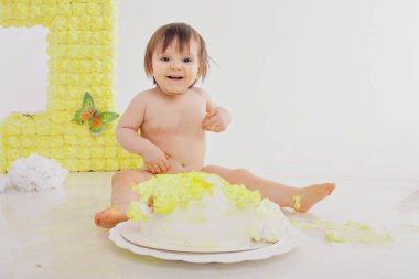 Küçük bir kız pastayı elleriyle şöminenin arka planında yer. Bebek yiyecekle kaplıydı. doğum günü partisi