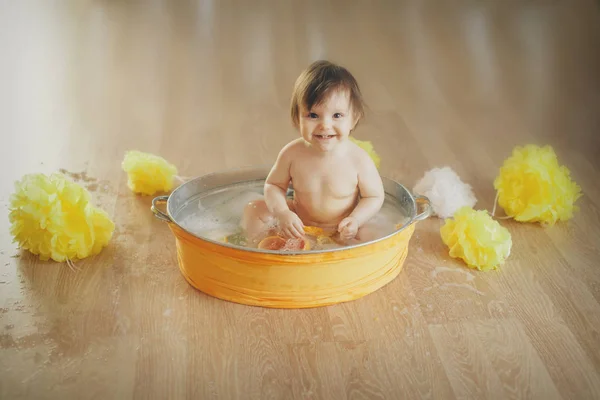 Een klein meisje baadt in een bad met citroen en grapefruit. Een kind wast zich in een bassin tussen gele bloemen. concept van kindertijd, gezondheidszorg, Ivf, hygiëne, citrustherapie — Stockfoto