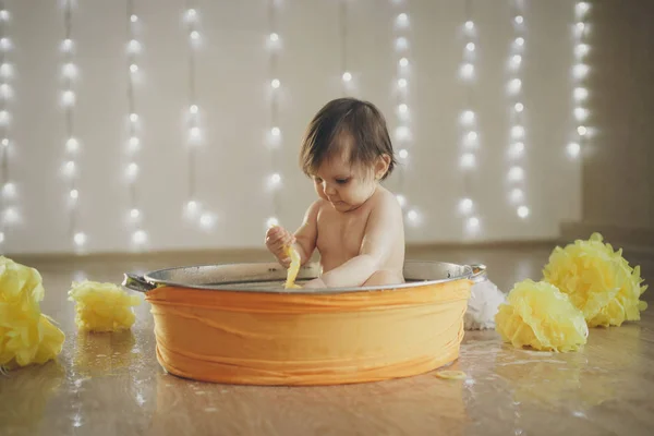 Uma menina está tomando banho em um banho com limão e toranja. Uma criança lava-se em uma bacia entre flores amarelas. conceito de infância, cuidados de saúde, FIV, higiene, terapia cítrica — Fotografia de Stock