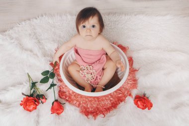 Küçük bir kız şöminenin yanında çiçeklerle banyo yapıyor. Kırmızı güllerin arasında bir çocuk havuzda yıkanır. Çocukluk konsepti, sağlık hizmeti, Ivf, hijyen, aroma terapisi