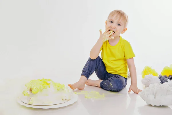 Um garotinho come bolo com as mãos no chão da lareira. A criança estava coberta de comida. festa de aniversário — Fotografia de Stock