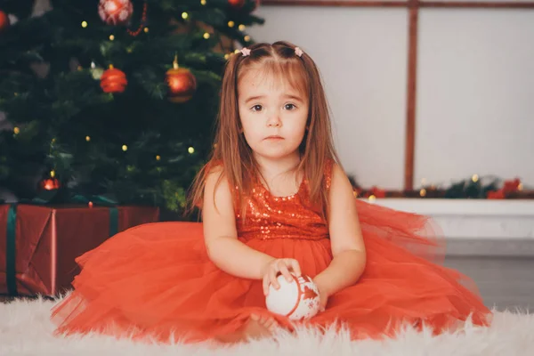 Small girl in red clothes with snow ball in hand under the Christmas tree. the concept of celebrating Christmas ,midnight, new year, — Stock Photo, Image