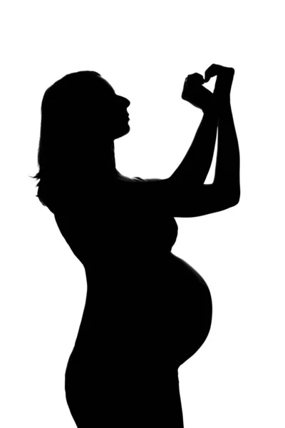 Silhouette di una donna incinta su sfondo bianco. La futura mamma mostra il segno del cuore con le mani. Il concetto di uno stile di vita sano, fecondazione in vitro, espressione di emozioni, gesti. Copia spazio — Foto Stock