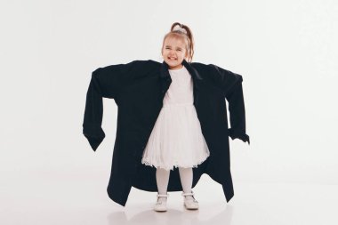 a little girl tries on dad's shirt. Child in big black clothes on white background. Concept of children's games, imitation of adult life, fashion clipart