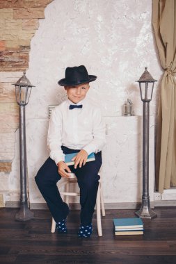 Çocuk kitap okuyor, sandalyede oturuyor. Eğitim. İç mekan: Lambalar, şapka