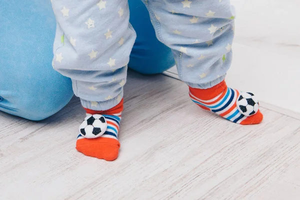 Tatlı bebek yürümeyi öğreniyor ve ilk adımlarını atıyor. Annem onun elini tutuyor. Çocuğun ayakları kapalı, kopyalama alanı, taşaklı çoraplar