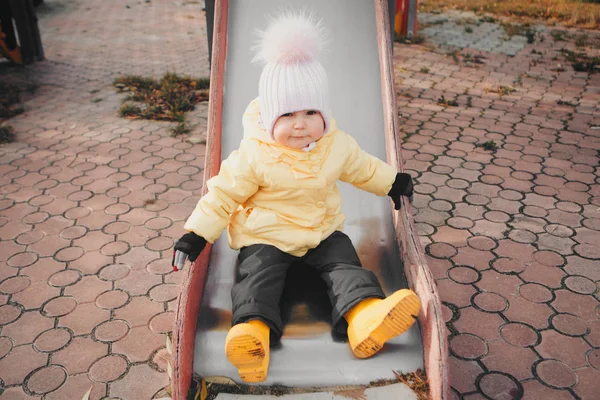 Une petite fille jouant sur l'aire de jeux de la ville des enfants. un petit enfant descend la colline, sur le carrousel, grimpe les cordes. Concept de l'industrie du divertissement, journée familiale, parcs pour enfants — Photo