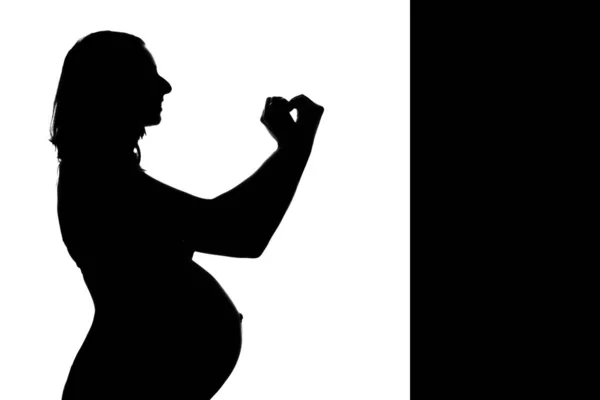 Silhueta de uma mulher grávida em um fundo branco. A gestante mostra o sinal do coração com as mãos. O conceito de um estilo de vida saudável, FIV, expressão de emoções, gestos. Espaço de cópia — Fotografia de Stock