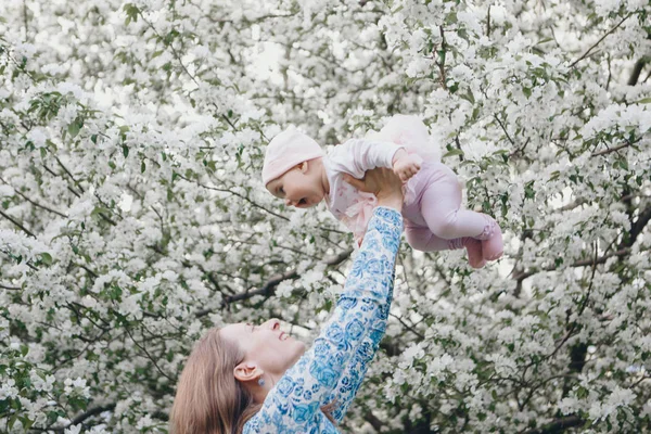 En vacker kvinna som håller barn. 8 mars: Kvinnor bland blommor. En flygande baby. Begreppet gratulationer, kvinnors helgdagar, naturlig make up — Stockfoto