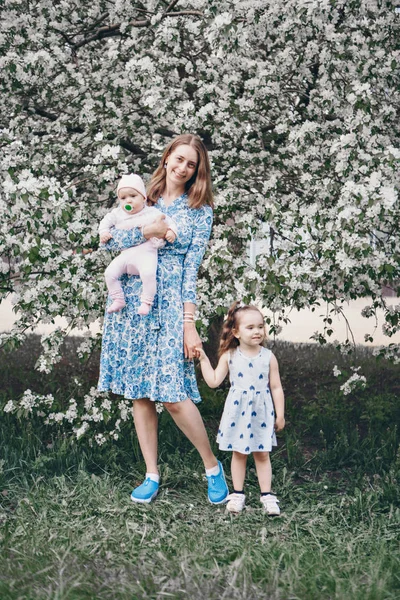 Vacker kvinna som håller barn. 8 mars: Kvinnor bland blommor. Begreppet gratulationer, kvinnors helgdagar, naturlig make up — Stockfoto