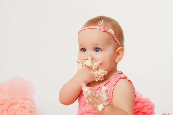 Menina comendo bolo com as mãos no fundo branco. A criança está coberta de comida. Estragou a doçura. O conceito de aniversário, feriados, culinária — Fotografia de Stock