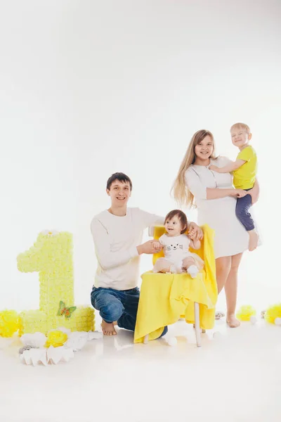 Святкування дня народження: сім'я сидить на підлозі серед прикрас: цифри 1, штучні квіти та білі кульки — стокове фото