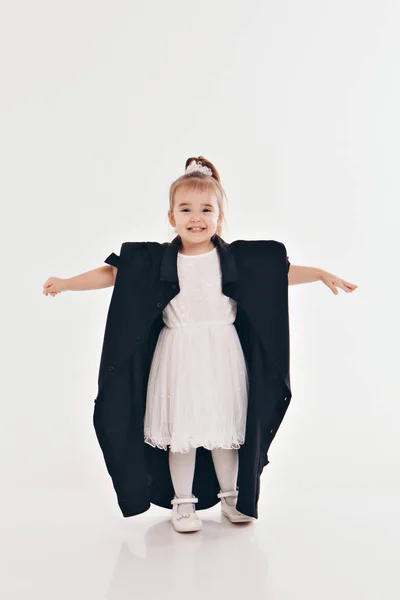 A little girl tries on dad's shirt. Child in big black clothes on white background. Concept of children's games, imitation of adult life, fashion — Stock Photo, Image