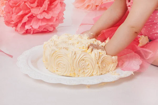 Menina comendo bolo com as mãos no fundo branco. A criança está coberta de comida. Estragou a doçura. O conceito de aniversário, feriados, culinária — Fotografia de Stock