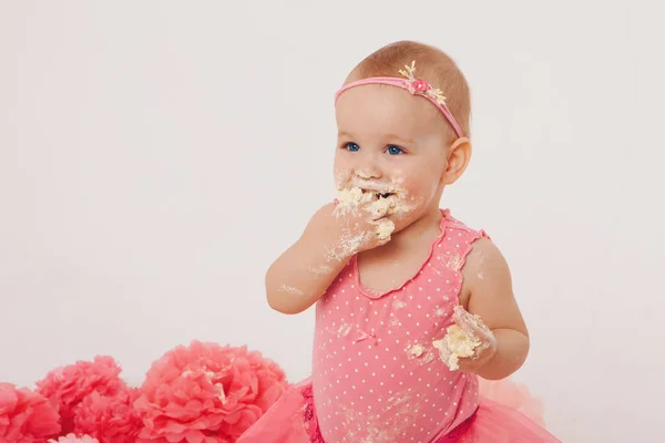 Menina comendo bolo com as mãos no fundo branco. A criança está coberta de comida. Estragou a doçura. O conceito de aniversário, feriados, culinária — Fotografia de Stock