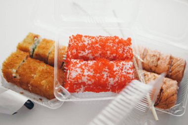 Japon mutfağı: plastik bir kapta rulo. Beyaz arka planda suşi. Geleneksel Doğu mutfağı reklam kavramı, balık yemi: somon, ton balığı, pirinç