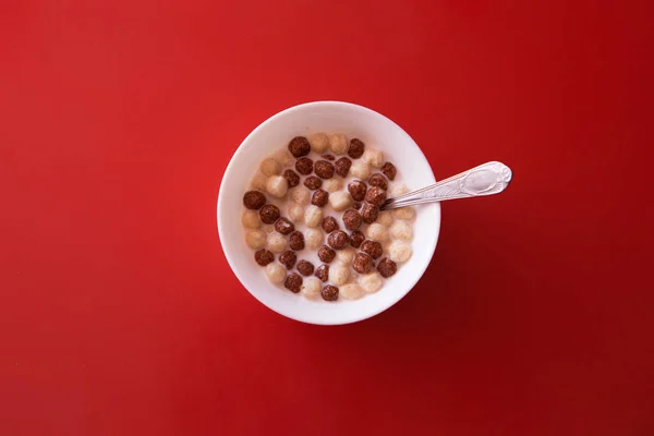 El concepto de un delicioso y saludable desayuno, comida saludable, la publicidad de bolas de chocolate con leche. plato, comida para bebés y leche sobre fondo rojo. Copiar espacio —  Fotos de Stock