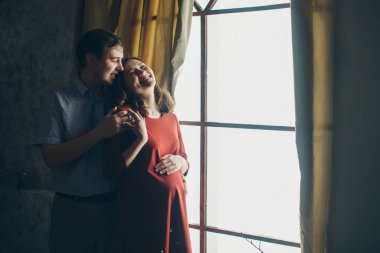 Sevgi dolu bir çift pencerede kucaklaşır. Bir erkek ve bir kadın birbirlerinin gözlerinin içine bakar. Koca hamile karısına sarılıyor ve karnını okşuyor. Sevgililer Günü. 14 Şubat