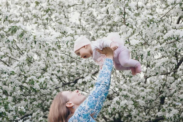 Vacker kvinna som håller barn. 8 mars: Kvinnor bland blommor. Begreppet gratulationer, kvinnors helgdagar, naturlig make up — Stockfoto