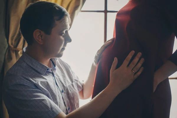 Ein liebendes Paar umarmt sich am Fenster. ein Mann und eine Frau schauen einander in die Augen. umarmt der Ehemann seine schwangere Frau und streicht über ihren Bauch. Valentinstag. 14. Februar — Stockfoto