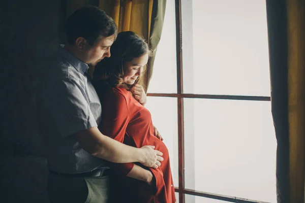 사랑하는 한 부부가 창밖을 내다보며 이렇게 말합니다. 한 남자와 한 여자가 서로 의 눈을 들여다 봅니다. 남편은 임신 한 아내를 껴안고 아내의 배를 때리고 있다. 발렌타인데이. 2 월 14 일 — 스톡 사진