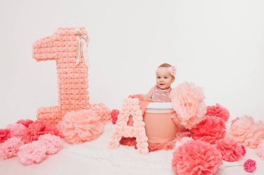 Doğum günü kutlaması: çocuk yerde madalyonun yanında oturuyor: 1 numara, yapay çiçekler ve hediyeler. Doğum günü konsepti, tatiller. Boşluğu kopyala