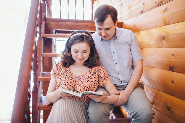 愛情のある夫婦が階段で抱擁する男と女が互いの目を見る。夫は妊娠中の妻を抱きかかえて本を読む。バレンタインデーだ2月14日 — ストック写真